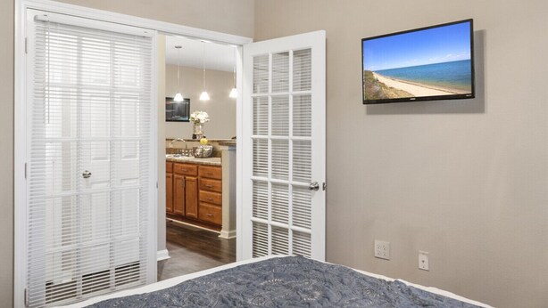 Une chambre à coucher avec un lit, un téléviseur fixé au mur et une armoire avec des volets blancs.