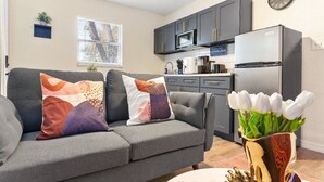 Ein modernes Wohnzimmer mit einem grauen Sofa, bunten Kissen, einem Couchtisch und einer Vase mit weißen Tulpen.