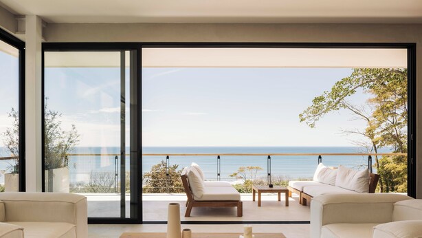 A modern living room with a large glass door leading to a balcony with a view of the sea. There are two sofas, a coffee table, and a small table with candles. - Unique luxury Ocean view villa steps from the beach (Cóbano)