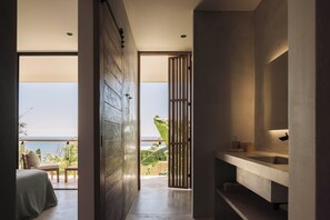 Une salle de bain moderne dotée d’un grand miroir, d’un plan de toilette et offrant une vue sur l’océan grâce à une porte coulissante.