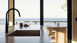 A modern kitchen with a large window overlooking the ocean, a wooden dining area, and a minimalist design. - Unique luxury Ocean view villa steps from the beach (Cóbano)