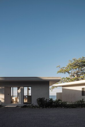 Une maison moderne dotée d’une grande porte vitrée donnant sur un patio, une petite piscine et offrant une vue sur l’océan.