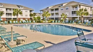 A pool area with lounge chairs and a swimming pool, surrounded by multi-story buildings with balconies.