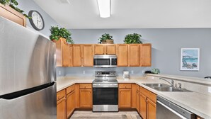A modern kitchen with stainless steel appliances, wooden cabinets, and a beach-themed artwork on the wall.