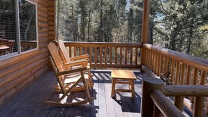 A wooden deck with a rocking chair and a small table, overlooking a forested area.