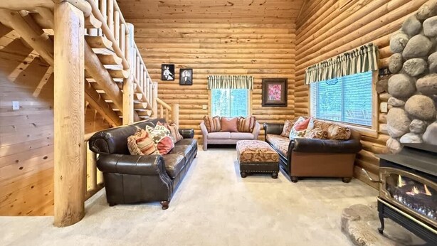 A log cabin interior with a staircase, two sofas, a fireplace, and a stone wall.