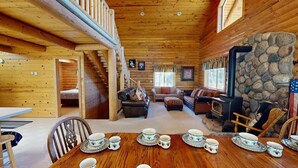 A cozy log cabin interior with a dining area set for tea, a fireplace, and a stone wall.