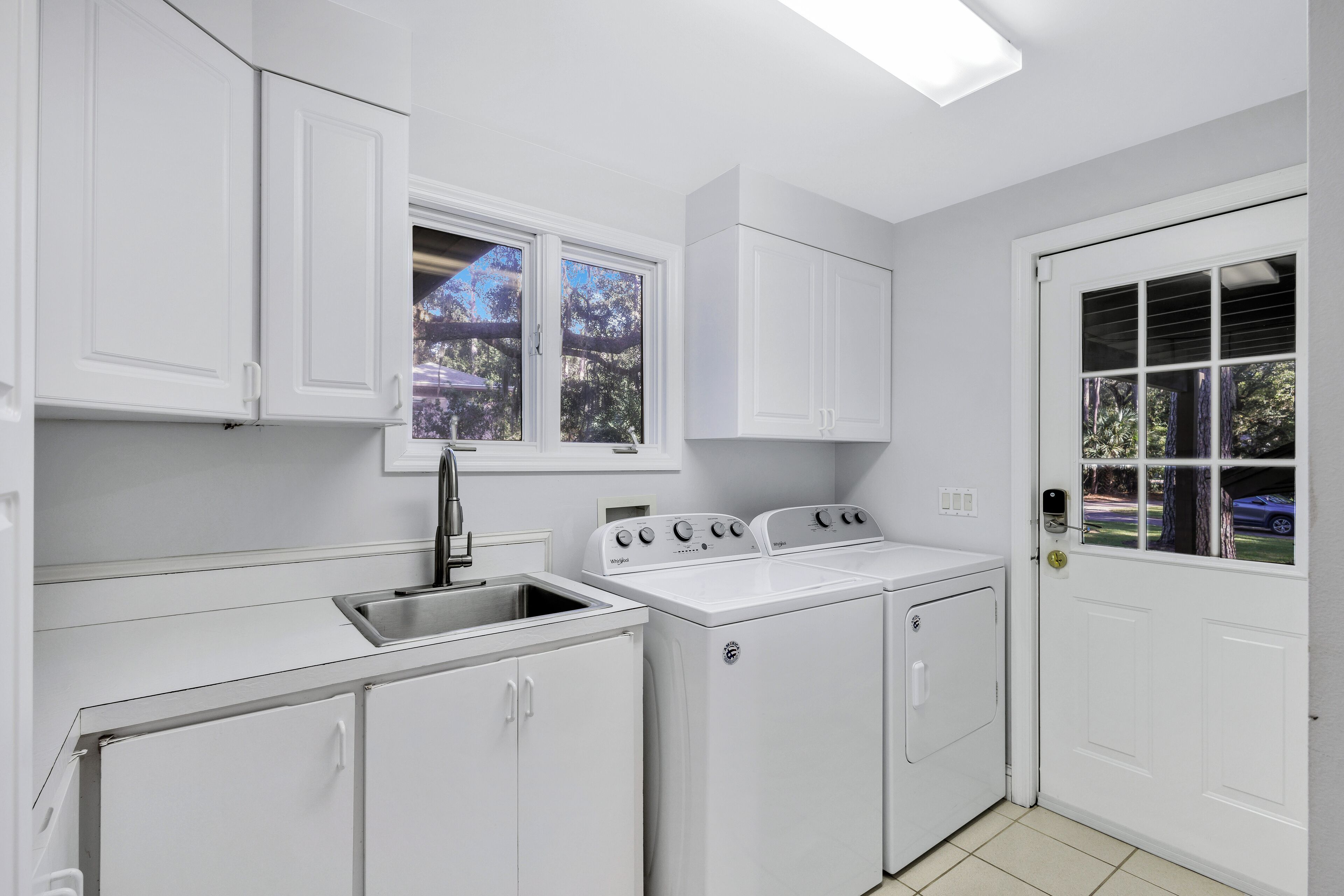 A laundry room with white cabinets, a sink, and two washing machines.