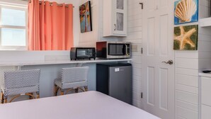 A compact room with a bed, a kitchenette with a microwave, a refrigerator, and two wicker chairs.