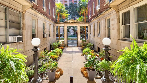 Une cour intérieure avec un chemin central bordé de plantes en pot et un bâtiment en briques en arrière-plan.