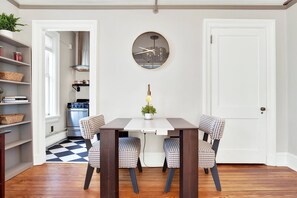 Een eethoek met een tafel, twee stoelen, een potplant en een klok aan de muur.