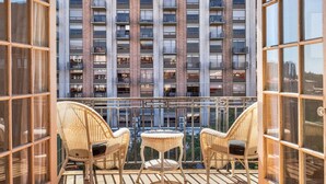 Un balcon agrémenté de fauteuils en osier et d’une petite table, d’où l’on peut admirer un immeuble de grande hauteur doté de nombreux balcons.