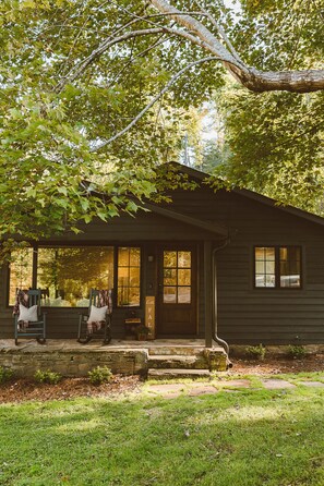 A cabin with a porch, stone steps, and a view of the surrounding forest. - Dudley Creek Cottage; cozy little cottage. Hot tub + fire pit + arcade!  (Gatlinburg)