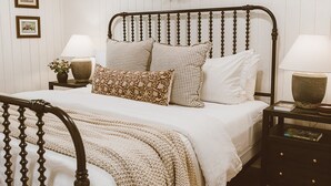 Un dormitorio ordenado con una cama, mesitas de noche y una corona decorativa en la pared.