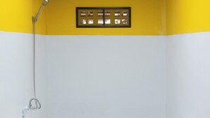 Un baño con decoración en tonos amarillo y blanco, un cabezal de ducha y una rejilla de ventilación.