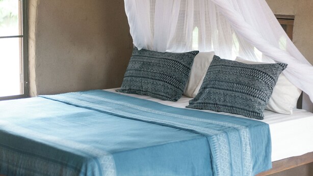 Una cama con dosel, ropa de cama azul y almohadas estampadas.