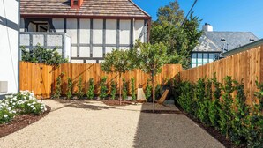 Un patio trasero residencial con camino de grava, valla de madera y pequeños árboles.