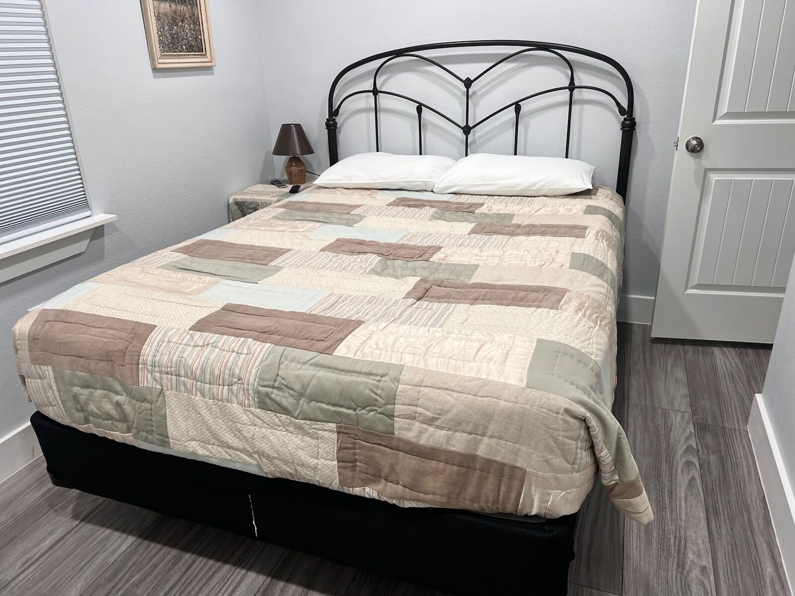 A bed with a quilt, a nightstand with a lamp, and a door.