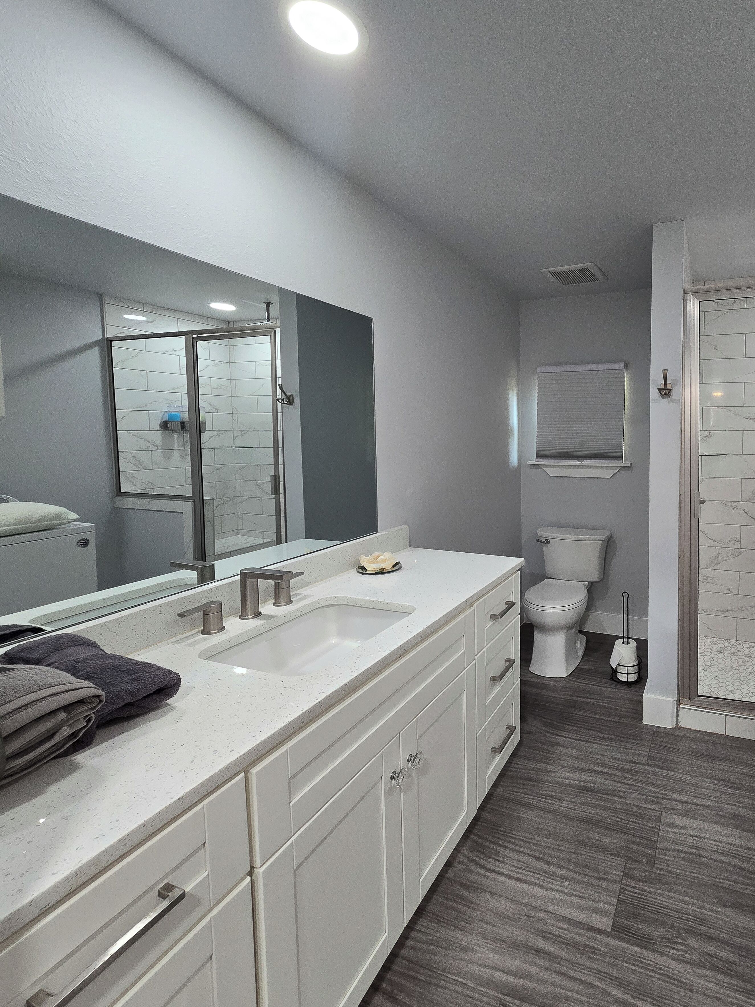 Un baño moderno con un espejo grande, tocador blanco y zona de ducha.