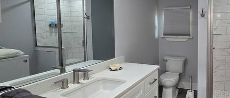 Un baño moderno con un espejo grande, tocador blanco y zona de ducha.