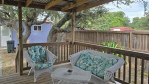 A covered outdoor deck with wicker furniture and a wooden railing. - Charming 3-bedroom cottage in serene Aransas Pass with AC, WiFi (Aransas Pass)