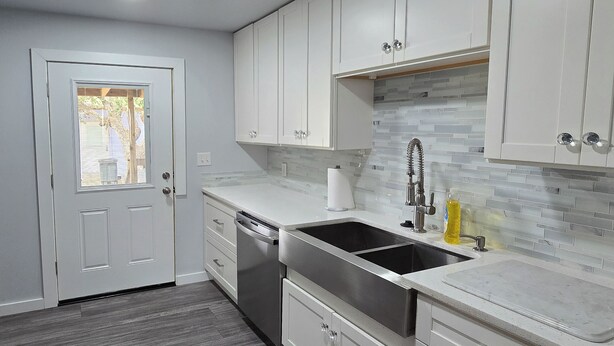 A modern kitchen with white cabinetry, a stainless steel sink, and a tiled backsplash. - Charming 3-bedroom cottage in serene Aransas Pass with AC, WiFi (Aransas Pass)