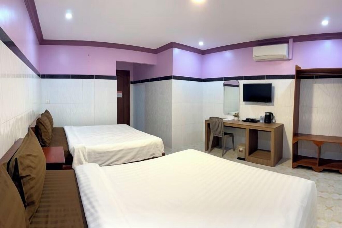 A hotel room with two beds, a desk, a chair, a television, and an air conditioning unit.