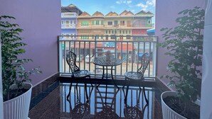 A balcony with a table and chairs, potted plants, and a view of colorful buildings. - The Cozy Corner-Budget Hotel (Kampot)