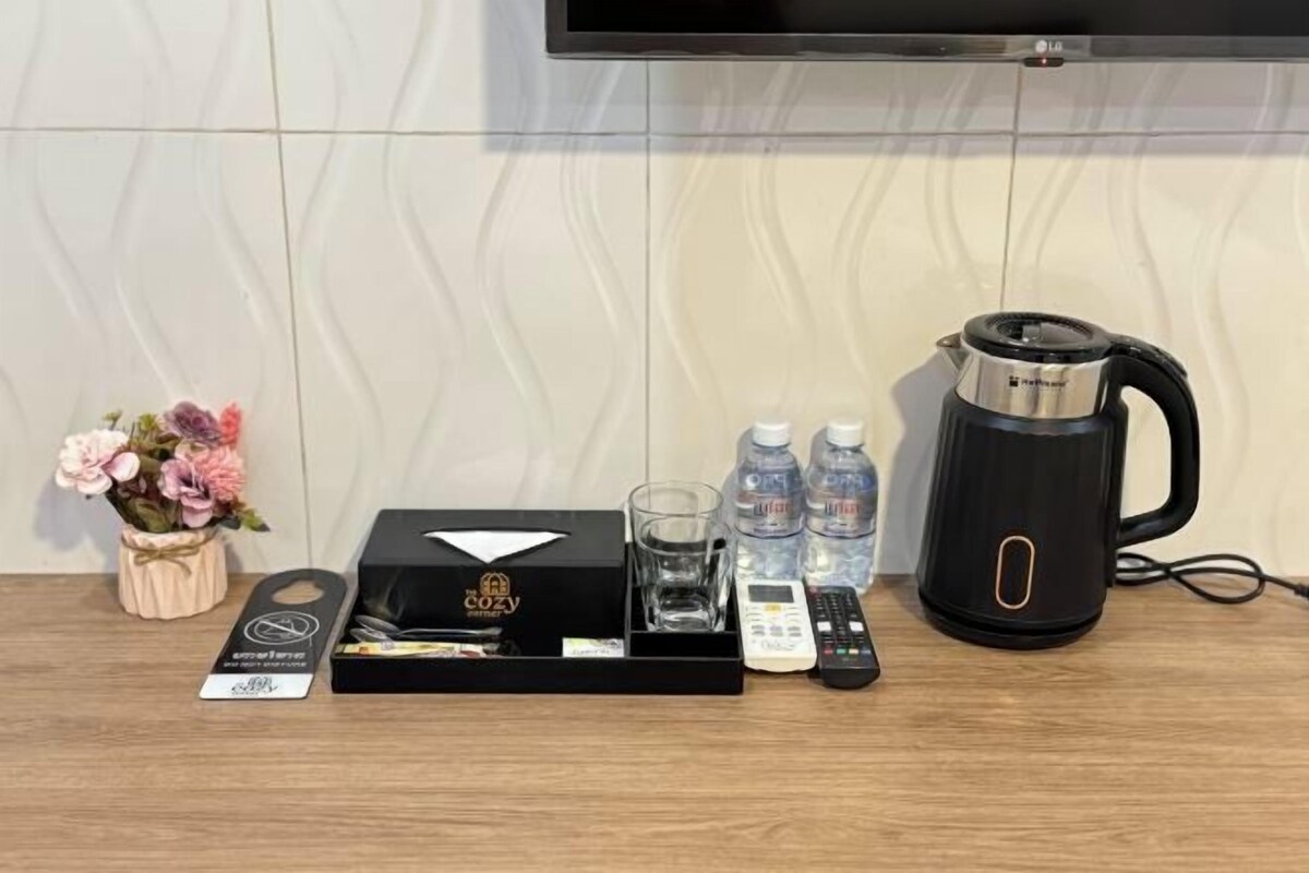 A hotel room with a flat-screen TV mounted on the wall, a black coffee maker, a tray with a box of tissues, two glasses, two bottles of water, and a remote control.