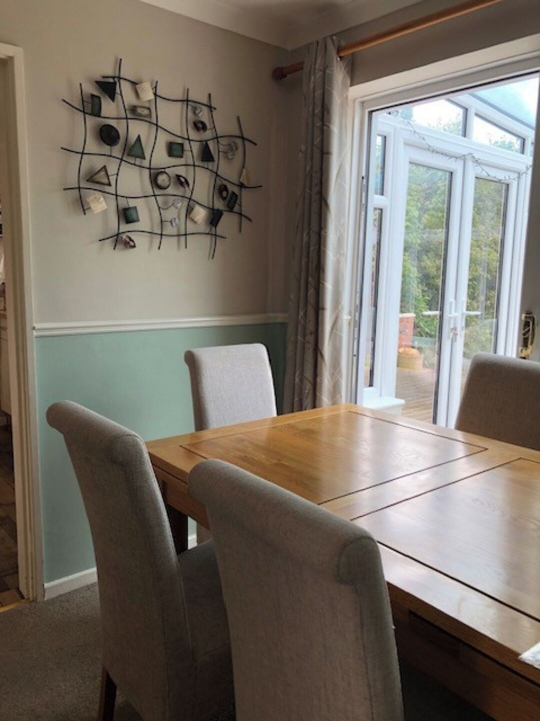 Un comedor con una mesa de madera y cuatro sillas grises. Se observa una obra de arte abstracta colgada en la pared sobre la mesa.
