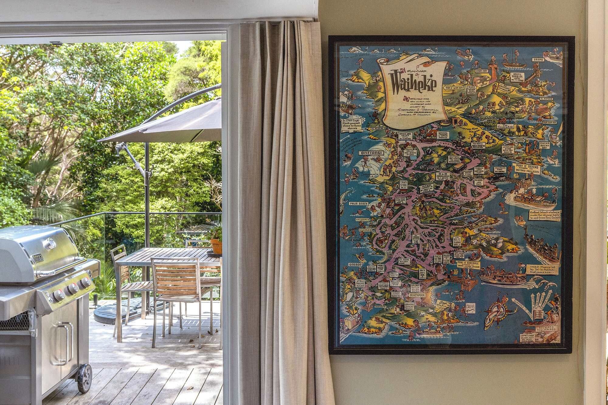 Een inlijst kaart van Waikiki aan een muur, een barbecue en een patio tafel met stoelen.