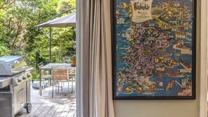 A framed map of Waikiki on a wall, a grill, and a patio table with chairs. - Hillside Hideaway - Our Island (Waiheke Island)