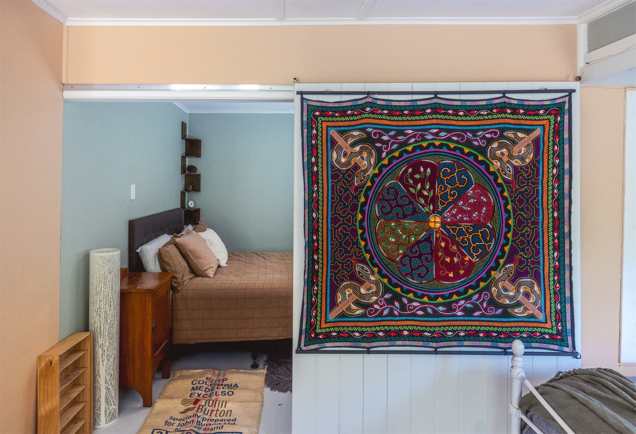 A bedroom with a bed, a nightstand, a lamp, a wall tapestry, and a window.