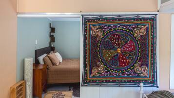 A bedroom with a bed, a nightstand, a lamp, a wall tapestry, and a window.