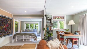 A spacious room with a bed, a dining area, and a large window providing natural light. - Hillside Hideaway - Our Island (Waiheke Island)
