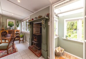 A cozy room with a fireplace, a dining area, and a window with a view of greenery. - Hillside Hideaway – Magical Cottage Escape (Waiheke Island)
