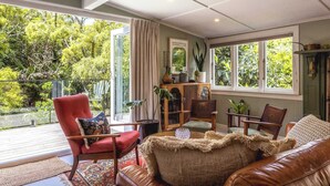A cozy living room with a red armchair, a brown leather sofa, and a wooden cabinet with plants. - Hillside Hideaway - Our Island (Waiheke Island)
