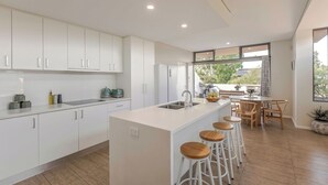 Une cuisine moderne avec des meubles blancs, un îlot central doté de tabourets et un coin repas avec des chaises et une table en bois.