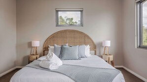 Une chambre à coucher bien aménagée, avec un grand lit, deux tables de chevet avec des lampes, une fenêtre donnant sur les arbres et une petite fenêtre située au-dessus du lit.