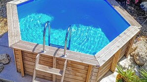 A wooden hot tub with two metal ladders, surrounded by pebbles and plants.