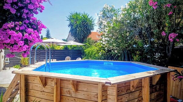 A wooden swimming pool with a ladder, surrounded by lush greenery and flowering plants.