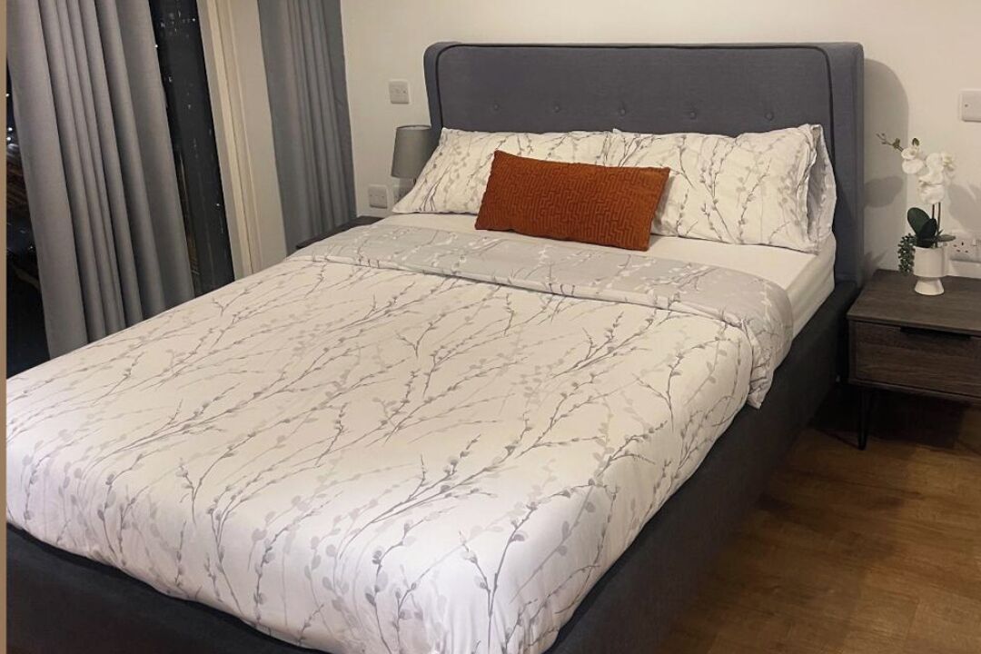 En snyggt bäddad säng med ett mönstrat överkast och två kuddar, ett sängbord med en lampa och en liten växt på bordet.