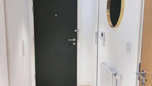 Un intérieur moderne avec une porte noire, un mur blanc orné d’un miroir rond et un plancher en bois.