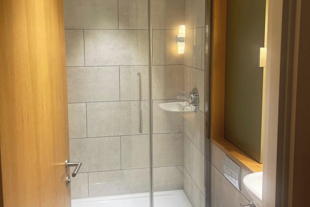 Een moderne badkamer met een douchecabine van glas, een wastafel en een spiegel.