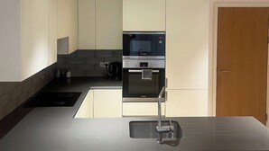 Une cuisine moderne dotée d’un four et d’un micro-ondes encastrés, d’un évier en acier inoxydable et d’une porte en bois.