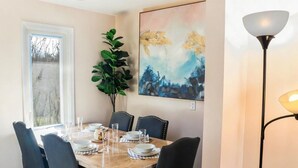 A dining room with a wooden table set for four, surrounded by chairs. A large abstract painting is on the wall, and a floor lamp is visible to the right. - Entire house 3BR, Pets, kitchen, Parking, Laundry, Large Fenced backyard, WiFi (Kitchener)