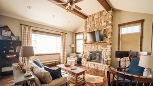 A cozy living room with a stone fireplace, wooden furniture, and large windows.