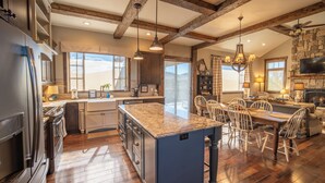 A spacious kitchen with a large island, wooden beams, and a stone fireplace.
