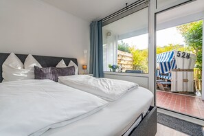 Habitación de hotel moderna con una cama grande, una mesita de noche, una ventana con cortinas y vistas al área de estar al aire libre.