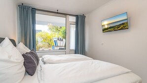 A hotel room with a bed, a window with curtains, and a painting of a beach scene. - This one love - Cozy vacation apartment for up to 3 people in Alt (Sylt)